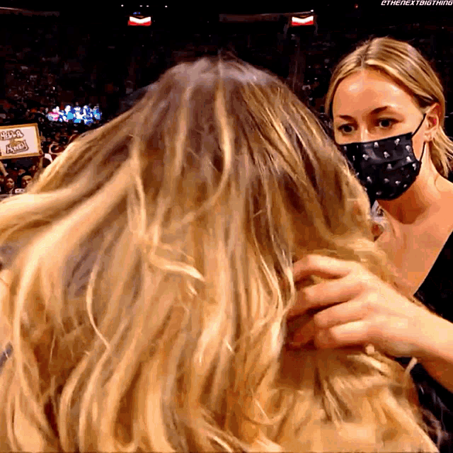 a woman wearing a mask holds another woman 's hair in front of a sign that says nba on it
