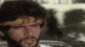 a man with a beard and a headband on his head is making a funny face .