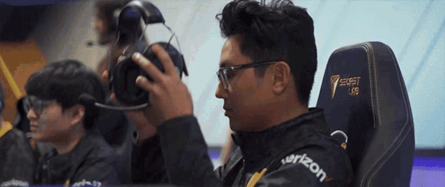 a man wearing glasses and headphones is sitting in a verizon gaming chair