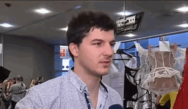 a man in a blue shirt is talking into a microphone in a room with clothes on display .