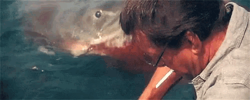 a man is smoking a cigarette in front of a large shark in the ocean .