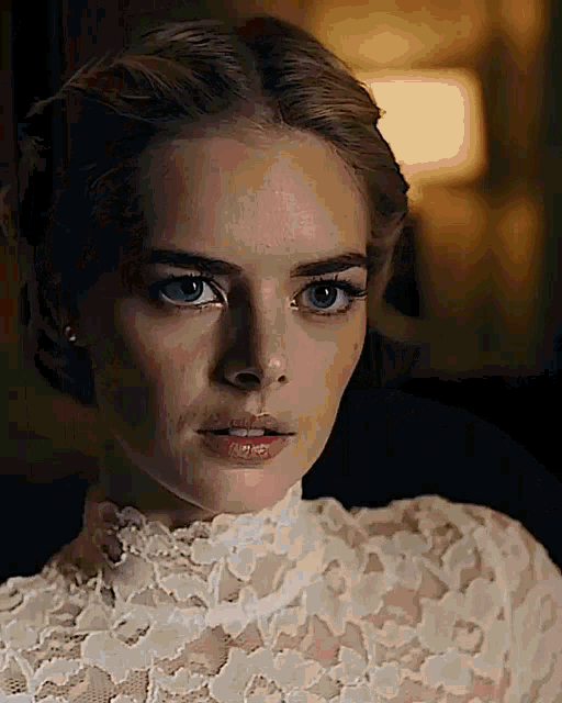 a woman is wearing a white lace top and earrings