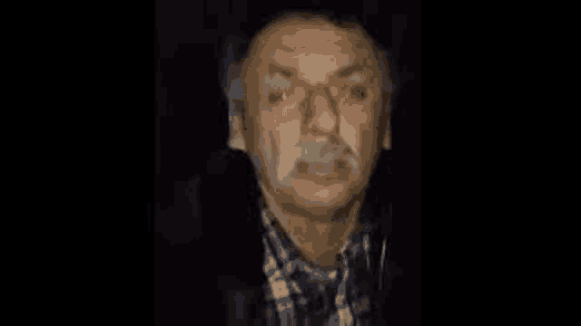 a man with a mustache and glasses is standing in the dark .