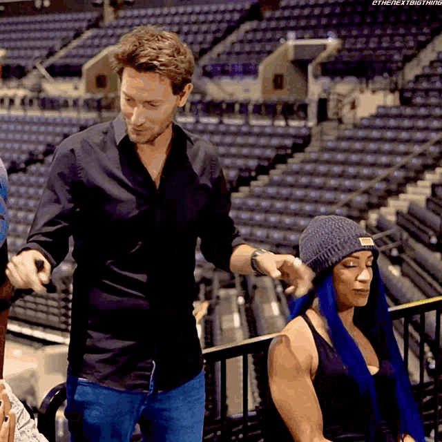 a man in a black shirt is standing next to a woman with blue hair in a stadium