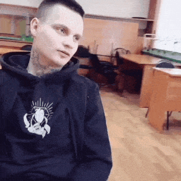 a man with a tattoo on his neck is wearing a black hoodie with a praying hands logo on it