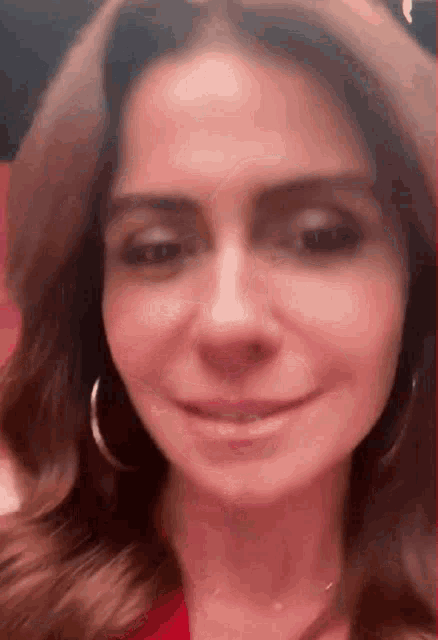 a close up of a woman 's face wearing hoop earrings and a red jacket .