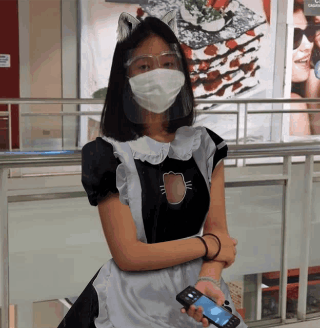 a woman wearing a mask and a maid outfit holds a cell phone