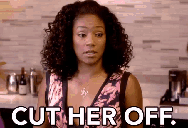 a woman with curly hair is standing in a kitchen with the words cut her off .