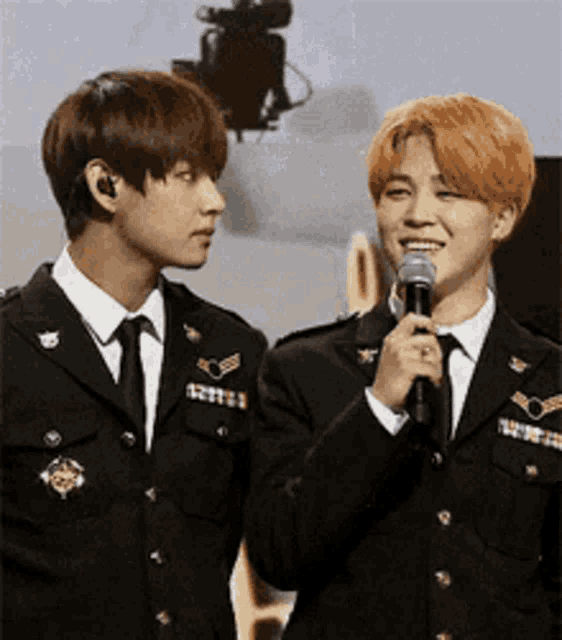 two men in military uniforms are standing next to each other and one is holding a microphone