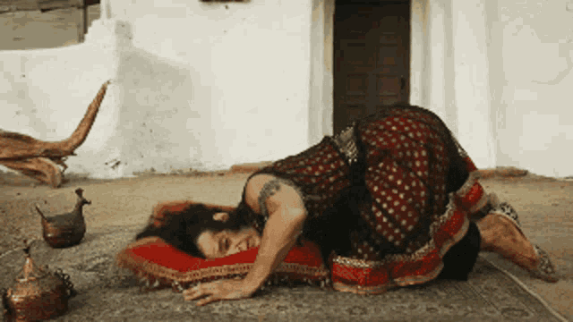 a woman in a red and gold dress is laying on a red pillow
