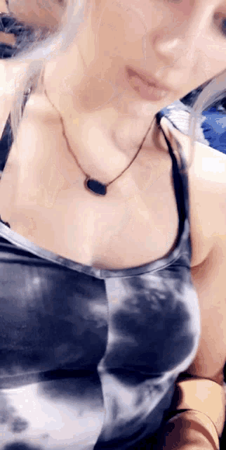 a woman wearing a tie dye tank top and a necklace is taking a picture of herself .