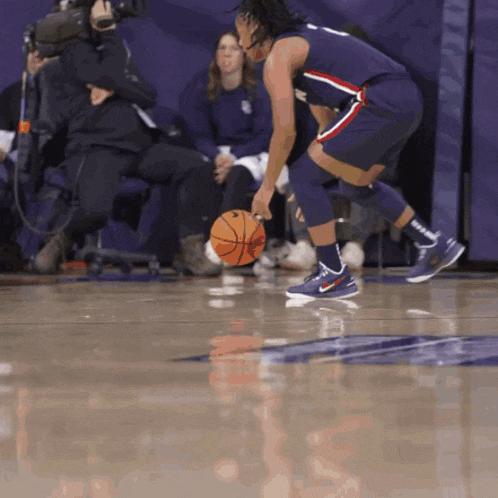 a basketball player dribbles a basketball on a court with a cameraman behind him
