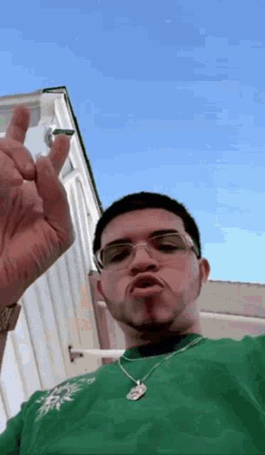 a man wearing glasses and a green shirt is making a face with his hand
