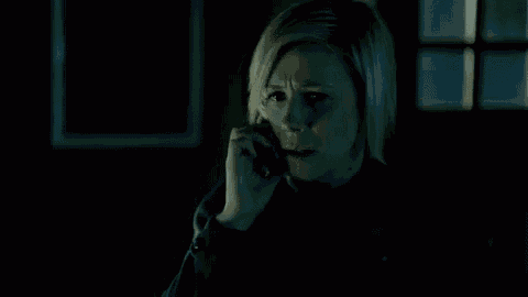 a woman is covering her mouth with her hands in a dark room while talking on a cell phone .