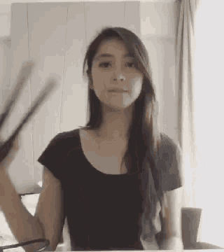 a woman in a black shirt is holding a pair of chopsticks in front of her face .