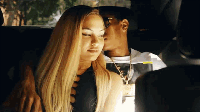 a man kisses a woman on the cheek while wearing a necklace that says lust