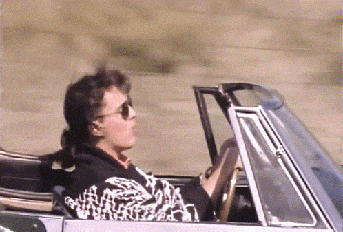 a man wearing sunglasses is driving a car with the top down