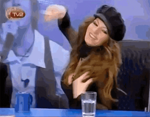 a woman is sitting at a table with a glass of water and a tv2 logo in the background .