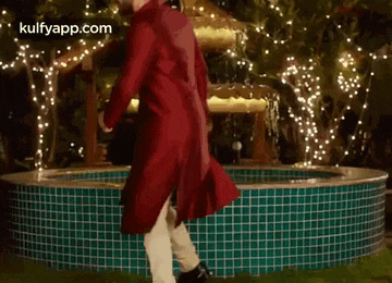 a man in a red dress is dancing in front of a water fountain .