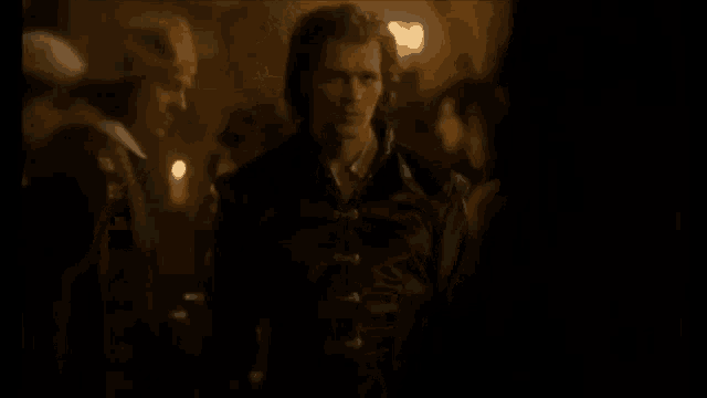a man in a leather jacket is standing in a dark room looking at a woman .