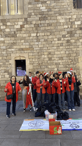 a group of people are standing in front of a brick wall with a sign that says ' christmas ' on it