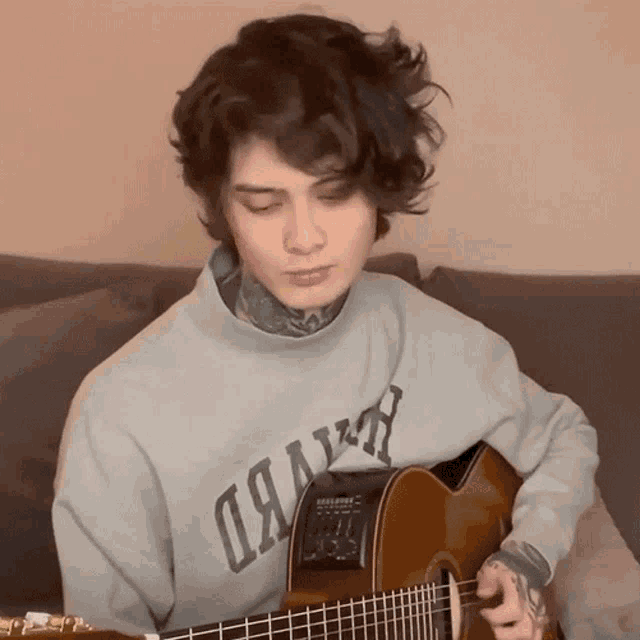 a young man playing a guitar wearing a grey sweatshirt that says ' oakland ' on the front