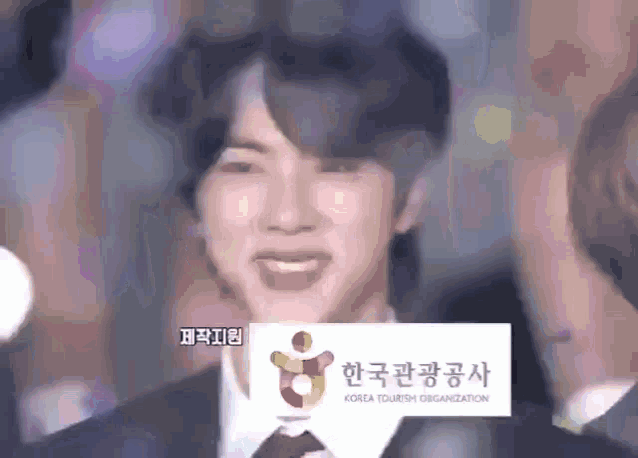a man in a suit and tie smiles in front of a sign that says korea tourism organization