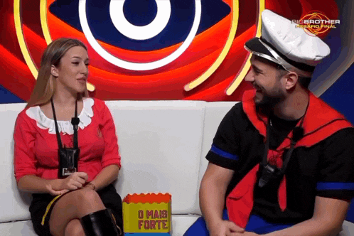 a man and woman are sitting on a couch with a box of popcorn that says o mais forte