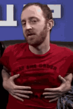 a man in a red shirt is holding his stomach with his hands .