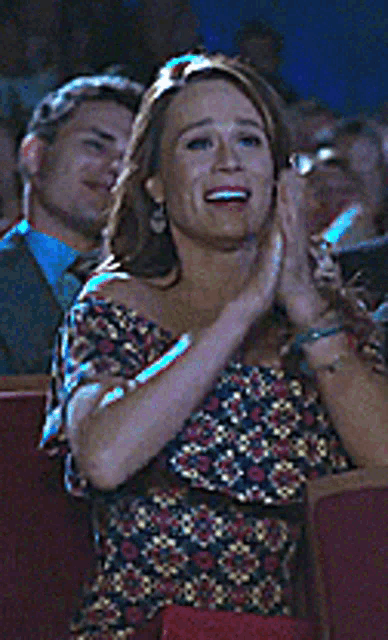 a woman in a floral top is clapping in a crowd