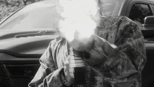 a black and white photo of a man holding a gun in front of a car .