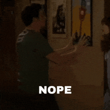 a man in a green shirt is standing in a room with the word nope written on the screen .
