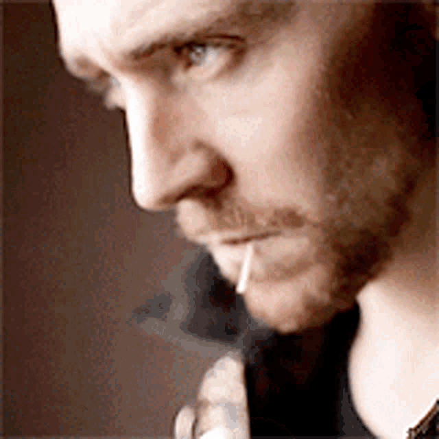 a close up of a man smoking a cigarette with a toothpick in his mouth