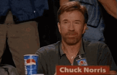 chuck norris is sitting at a table with a sign that says chuck norris