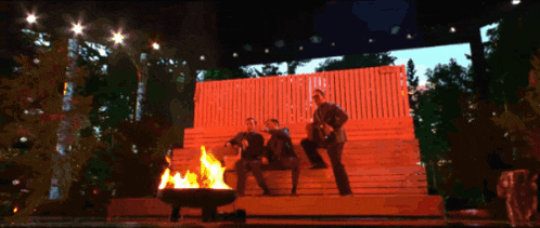 a group of people are sitting around a fire pit at night