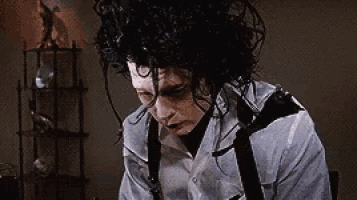 a man with curly hair is wearing a white shirt and suspenders and looking down .
