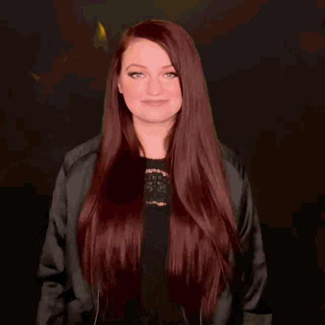 a woman with long red hair is wearing a black jacket and giving a thumbs up