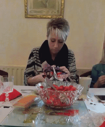 a woman sits at a table with a bowl of red flowers