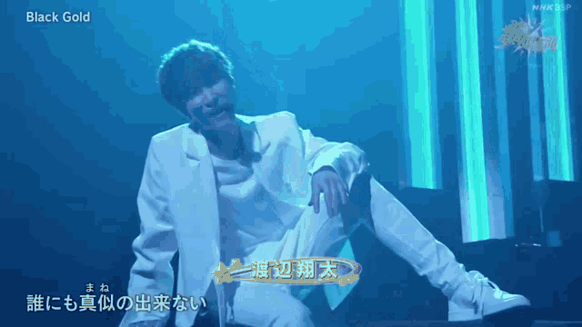 a man in a white suit is kneeling down on a stage with the words black gold on the bottom