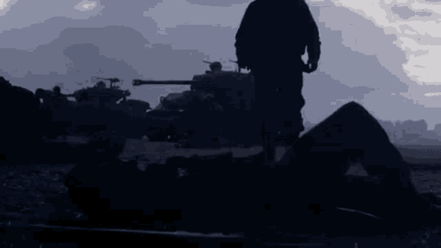 a soldier is standing in front of a row of tanks in a field .