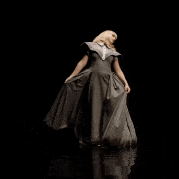 a woman in a long gray dress is standing in the dark
