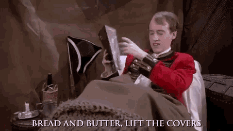 a man in a red uniform is reading a book while laying in a bed .
