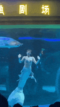 a woman dressed as a mermaid is swimming in an aquarium with chinese writing on the wall behind her