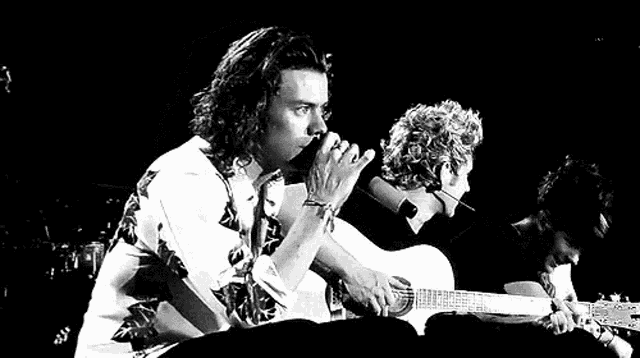a black and white photo of a man playing a guitar on a stage .