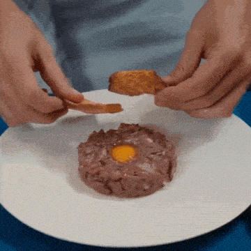 a person is holding a piece of bread over a plate of food