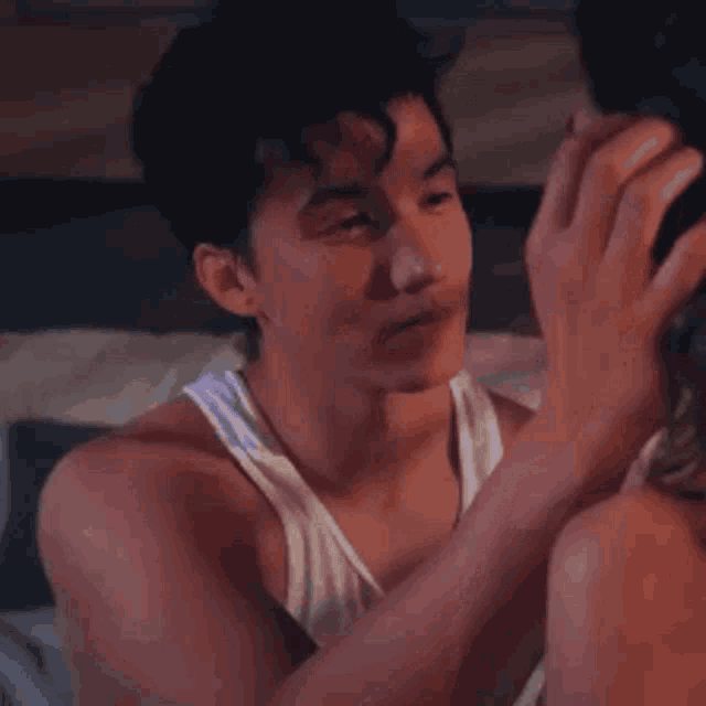 a man in a white tank top is touching a woman 's face while laying on a bed .