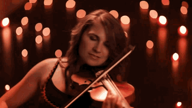 a woman is playing a violin in front of a bunch of red lights