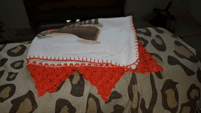 a white towel with a red crocheted border sits on a bed