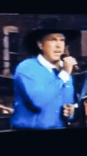 a man singing into a microphone wearing a blue jacket