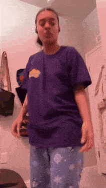 a woman in a purple shirt and blue pajamas is standing in a bathroom .